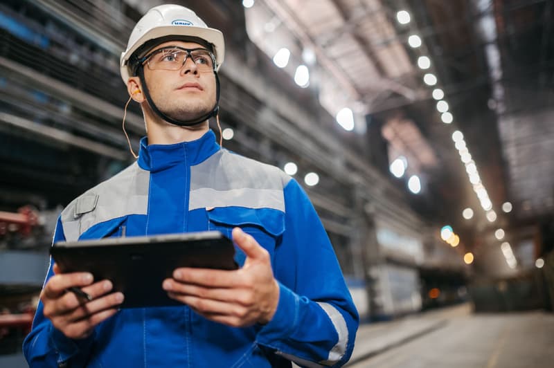 Mitarbeiter in Arbeitskleidung mit Tablet in einer Industriehalle